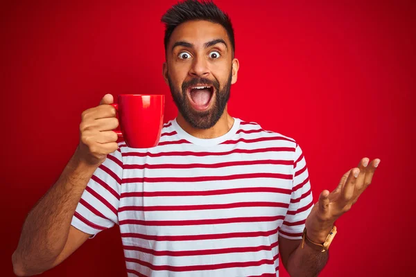 Молодой Индиец Полосатой Футболке Пьет Чашку Кофе Изолированном Красном Фоне — стоковое фото