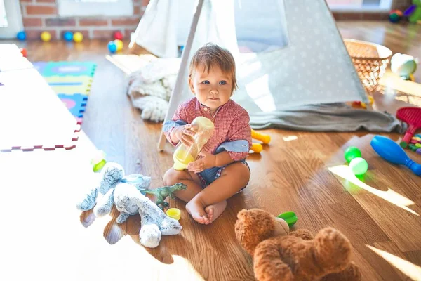 幼小可爱的幼儿在幼稚园里抱着奶瓶围着许多玩具 — 图库照片