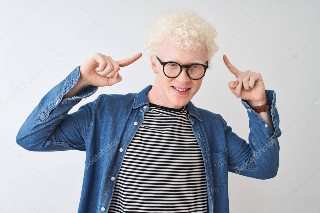 Young albino blond man wearing denim shirt and glasses over isolated white background smiling pointing to head with both hands finger, great idea or thought, good memory