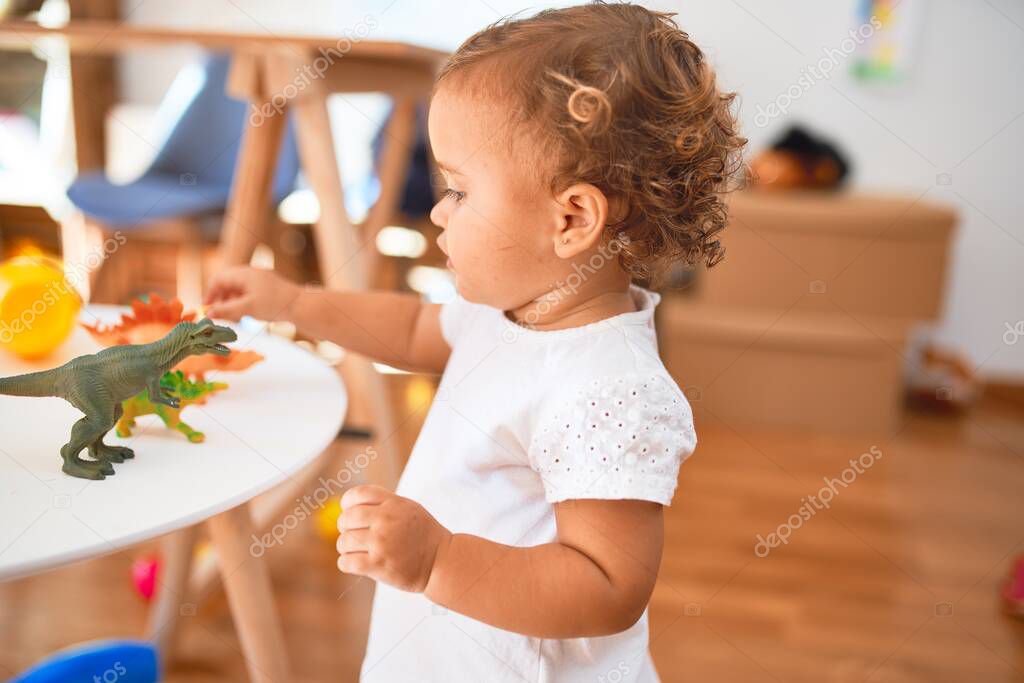 Adorable toddler playing with dinosaurs around lots of toys at kindergarten