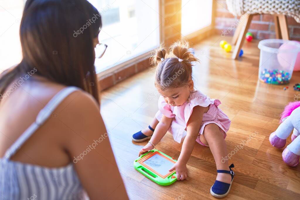 Young beautiful teacher and toddler drawing using digital board at kindergarten