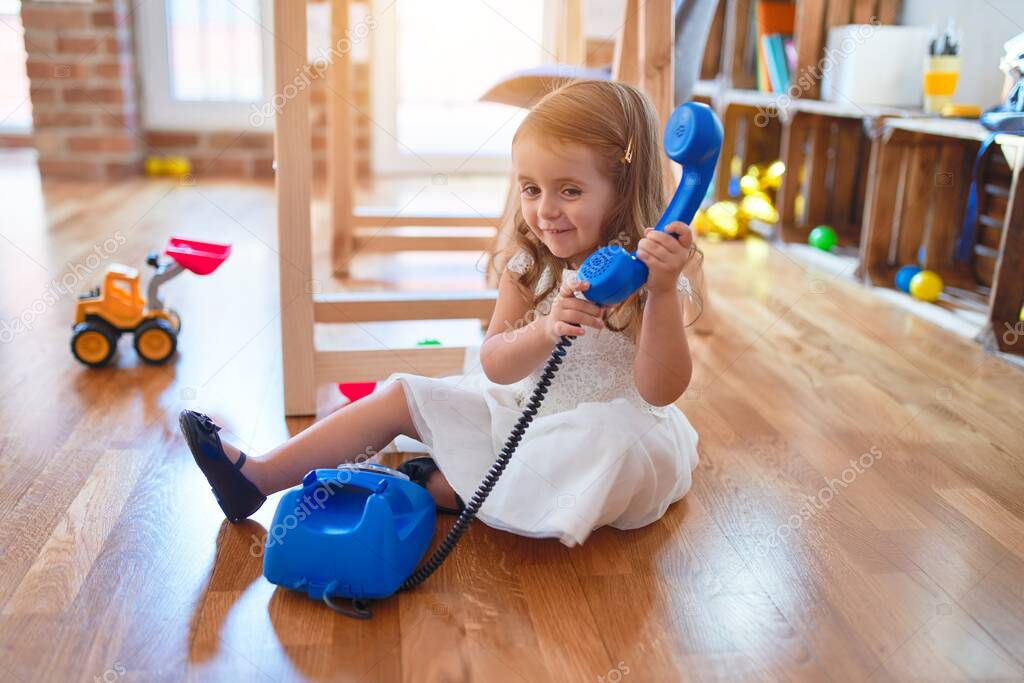 Adorable blonde toddler playing with vintage phone. Sitting on the floor around lots of toys at kindergarten