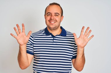 Sıradan çizgili polo giyen genç adam izole edilmiş beyaz arka planda duruyor ve on numaralı parmaklarıyla işaret ederken kendinden emin ve mutlu bir şekilde gülümsüyor..