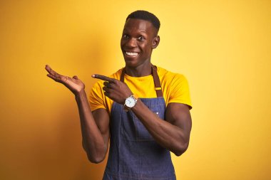 İzole edilmiş sarı arka planda duran önlük giyen Afrikalı Amerikalı barmen kameraya hayret ediyor ve gülümsüyordu..