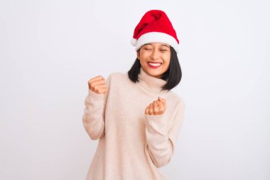 Noel Baba şapkası takan genç, güzel Çinli bir kadın izole edilmiş beyaz arka plan üzerinde çok mutlu ve heyecanlı bir şekilde kollarını kaldırıp, gülümseyerek ve başarı için çığlık atarak kazanan bir jest yapıyor. Kutlama konsepti.