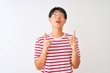 Genç Çinli gözlüklü ve çizgili tişörtlü bir adam izole edilmiş beyaz arka planda duruyordu. Şaşırmış ve şaşırmış bir şekilde yukarı bakıp parmaklarıyla işaret ediyor ve kollarını kaldırıyordu..