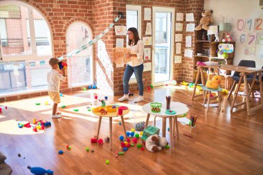 Anaokulunda bir sürü oyuncağın etrafında top ve hasır sepet kullanarak basketbol oynayan güzel öğretmen ve bebek.