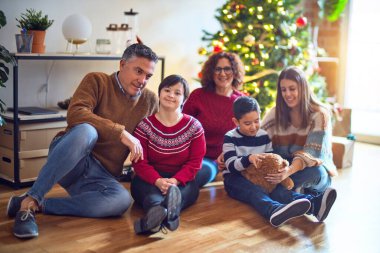 Mutlu ve kendinden emin gülümseyen güzel bir aile. Yerde oturup evde Noel ağacı etrafında poz vermek.