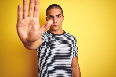 Sarı izole edilmiş arka planda çizgili tişört giyen yakışıklı genç adam avucunun içi gibi şarkı söylemeyi kesiyor. Yüzünde olumsuz ve ciddi bir jest olan uyarı ifadesi.
