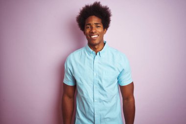 Afro saçlı, mavi gömlekli, mutlu ve havalı bir gülüşü olan, izole pembe arka planda duran genç bir Amerikalı. Şanslı kişi..