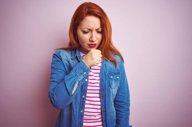 İzole edilmiş pembe arka plan üzerinde kot gömlek ve çizgili tişört giyen güzel kızıl saçlı kadın kendini kötü hissediyor ve soğuk algınlığı veya bronşitin belirtisi olarak öksürüyor. Sağlık hizmetleri kavramı.