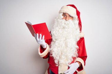 Orta yaşlı bir adam Noel Baba kostümü giyip izole edilmiş beyaz arka planda komik yüzlü yanakları şişiren kitap okuyor. Havayla şişmiş ağız, çılgın bir ifade..