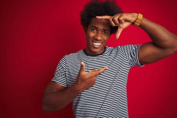 身穿海军条纹T恤的非洲裔美国年轻人在孤立的红色背景上微笑着 手指手画脚 面带笑容 创意和摄影概念 — 图库照片