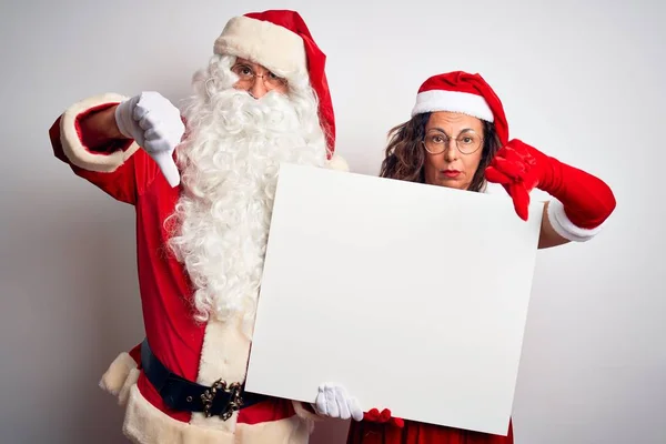 上了年纪的夫妇穿着圣诞老人的服装 拿着横幅盖住孤独的白色背景 满脸怒容 负面的迹象表明他们不喜欢大拇指朝下 拒绝的观念 — 图库照片