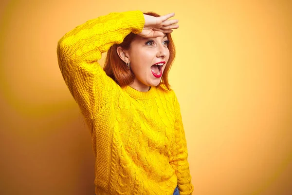 美しい赤毛の女性は 孤立した黄色の背景の上に立って冬のセーターを着て非常に幸せと笑みを浮かべて遠く離れて頭の上に手で見て 検索の概念 — ストック写真