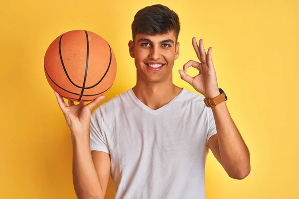 Молодой Индийский Спортсмен Держит Баскетбольный Мяч Стоя Изолированном Желтом Фоне — стоковое фото