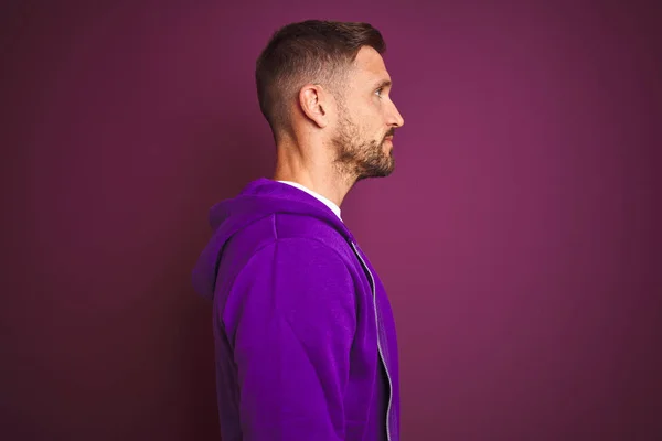 Young fitness man wearing casual sports sweatshirt over purple isolated background looking to side, relax profile pose with natural face with confident smile.
