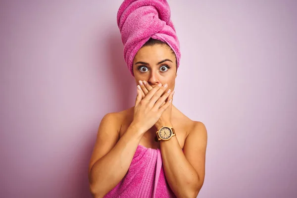 孤立したピンクの背景の上にシャワーの後のタオルを身に着けている若い美しい女性は間違いのための手で口を覆うショックを受けた 秘密概念 — ストック写真
