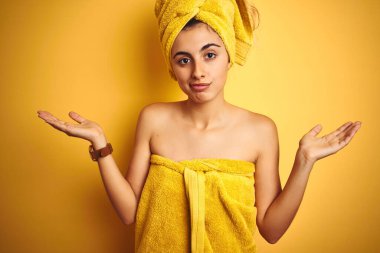 Sarıya boyanmış arka planda duş havlusu takan genç ve güzel bir kadın. Kolları ve elleri havada, kafası karışmış bir yüz ifadesi. Şüphe kavramı.