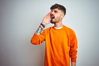 Turuncu süveter giyen genç adam izole edilmiş beyaz arka planda durup el ele tutuşarak bağırıyor ve bağırıyordu. İletişim konsepti.