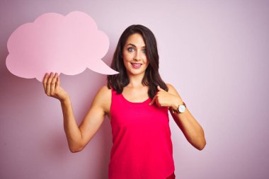 Beautiful woman holding speech bubble over pink isolated background with surprise face pointing finger to himself