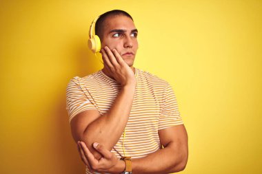 Sarıya boyanmış arka planda kulaklık kullanan genç yakışıklı bir adam. Elleri çenesinde soru sorarken, düşünceli bir ifade takınıyor. Düşünceli bir yüzle gülümsüyor. Şüphe kavramı.