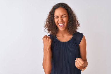 Mavi elbiseler giyen genç Brezilyalı bir kadın izole edilmiş beyaz arka planda mutlu ve heyecanlı bir şekilde kollarını kaldırıp, gülümseyerek ve başarı için çığlık atarak zafer jesti yapıyor. Kutlama konsepti.