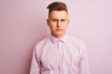 Soyutlanmış pembe arka plan üzerinde duran şık gömlekli genç yakışıklı işadamı şüpheci ve gergin, sorun yüzünden üzgün. Negatif kişi.