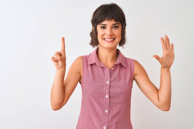 İzole edilmiş beyaz arka planda duran kırmızı tişörtlü genç ve güzel bir kadın. Altıncı parmaklarıyla işaret ederken kendinden emin ve mutlu gülümsüyor..