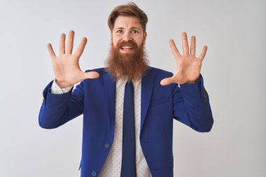 Genç, kızıl saçlı, takım elbiseli bir iş adamı izole edilmiş beyaz arka planda duruyor ve parmaklarını on numaraya doğrultuyor..