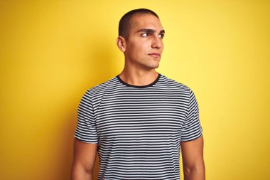 Sarı arka planda çizgili tişört giyen yakışıklı genç adam gülümsüyor ve başka tarafa bakıyor..