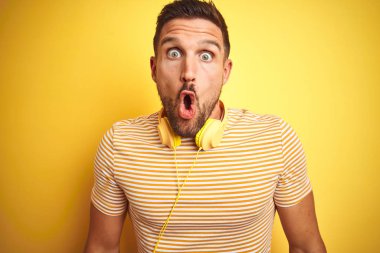 Kulaklık takan genç yakışıklı adam sarı arka planda müzik dinliyor. Korkmuş ve şok olmuş bir halde..