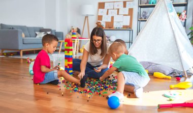 Anaokulundaki bir sürü oyuncağın etrafına taş döşeyen genç ve güzel öğretmenler ve yeni yürümeye başlayan çocuklar.
