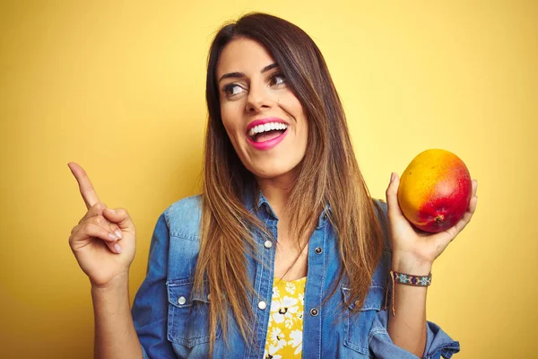 年轻美丽的女人在黄色的背景下吃着新鲜健康的芒果 非常快乐地手指手画脚 — 图库照片