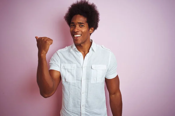 若いですアメリカ人男性とともにアフロ髪身に着けています白いシャツ上に立って隔離されたピンクの背景笑顔で幸せな顔を見て 親指アップで側面を指して — ストック写真