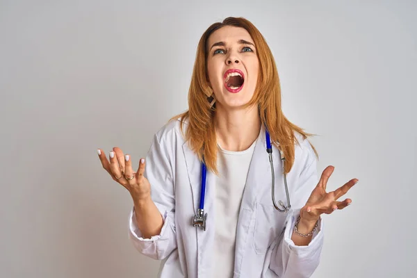 孤立した背景の上に聴診器を装着した赤毛の白人医師の女性は狂気と怒りの叫びと積極的な表情と腕を上げて叫んでいた 欲求不満の概念 — ストック写真