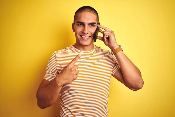 잘생긴 남자가 스마트폰으로 얘기하는 노란색외진 위에서 행복하게 손가락으로 가리키는 — 스톡 사진