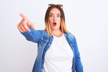 İzole edilmiş beyaz arka plan üzerinde duran kot gömlekli güzel bir kadın. Parmakla işaret ediyor. İleriye şaşırmış, ağzı açık, şaşırmış bir ifade.
