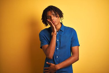 Rastgele kot gömlek giyen Afro bir adam izole edilmiş sarı arka planda duruyor. Kollarını kavuşturup depresyondan sıkılmış ve yorgun görünüyor..