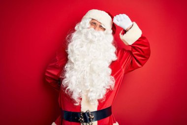 Orta yaşlı yakışıklı bir adam Noel Baba kostümü giyiyor. Kırmızı arka planda dikiliyor. Yorgun, rahat, uykulu ve sabahın erken saatlerinde esniyor.