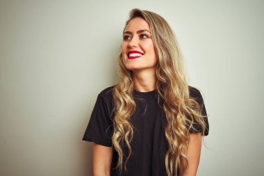 Siyah tişört giyen genç güzel bir kadın izole edilmiş beyaz arka plan üzerinde duruyor yüzünde gülümseme, doğal bir ifade ile yan yana bakıyor. Kendinden emin gülen.