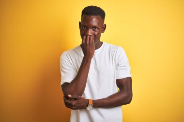 Beyaz t-shirt giyen genç Afro-Amerikalı adam izole edilmiş sarı arka planda dikiliyor. Elleri ağızdan tırnak yerken stresli ve gergin görünüyor. Endişe sorunu.