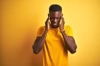 Genç Afro-Amerikalı bir adam günlük tişörtler giyiyordu. İzole edilmiş sarı arka planda duruyordu. Baş ağrısı vardı. Migren ağrısı..
