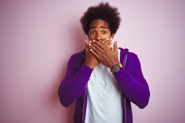 Mor eşofman üstü giyen genç Afro-Amerikalı adam izole edilmiş pembe arka planda dikiliyor. Ağzını yanlışlıkla ellerle kapatıyor. Gizli konsept.