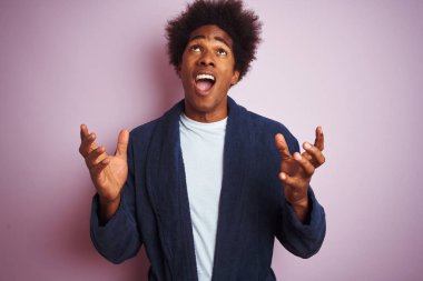 Genç Afro-Amerikalı pijama giymiş, pembe arka planda duran çılgın ve sinirli bir adam. Saldırgan bir ifade ve kollarla bağırıyor. Hayal kırıklığı konsepti.