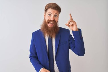 İzole edilmiş beyaz arka planda duran takım elbiseli genç kızıl saçlı işadamı başarılı bir fikir işaret ediyor. Heyecanlı ve mutlu. Bir numara..