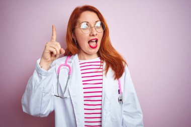 Pembe izole edilmiş arka planda gözlük takan genç kızıl saçlı kadın başarılı bir fikri işaret ediyor. Heyecanlı ve mutlu. Bir numara..