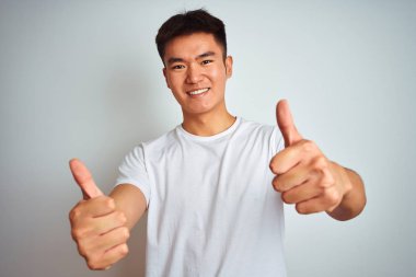 Asyalı genç bir Çinli erkek, izole edilmiş beyaz arka plan üzerinde durup el hareketini onaylıyor, gülümsüyor ve başarı için mutlu. Kazanan jest.