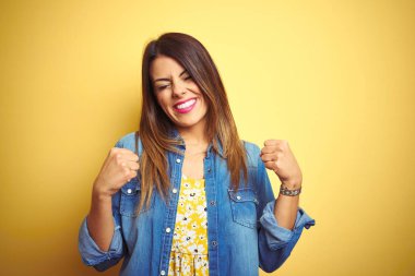 Sarı arka planda duran genç ve güzel bir kadın çok mutlu ve heyecanlı bir şekilde kollarını kaldırıp, gülümseyerek ve başarı çığlıkları atarak kazanan bir jest yapıyor. Kutlama konsepti.