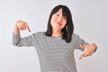 İzole edilmiş beyaz arka planda siyah çizgili tişört giyen genç, güzel Çinli kadın yüzünde bir gülümsemeyle, gururlu ve mutlu bir şekilde kendini işaret ediyor..